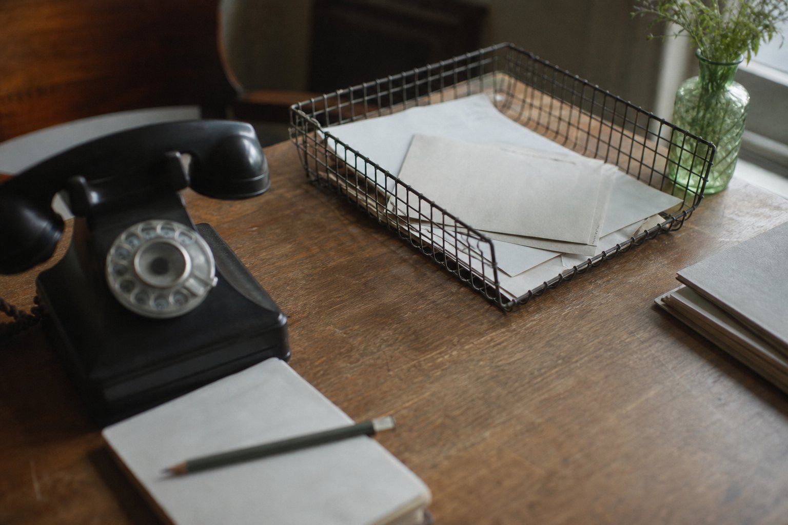 A desk corner with a wire letter tray, a black rotary telephone and a notepad