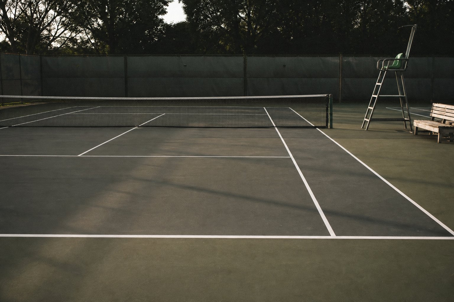 An empty hard tennis court photographed from behind the baseline, net taut, umpire chair to one side