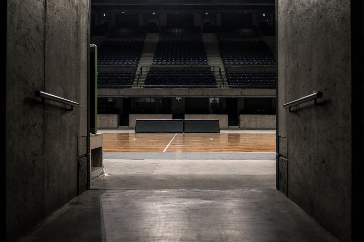 The mouth of a players' tunnel opening onto an empty basketball court, the folded scorer's table beyond