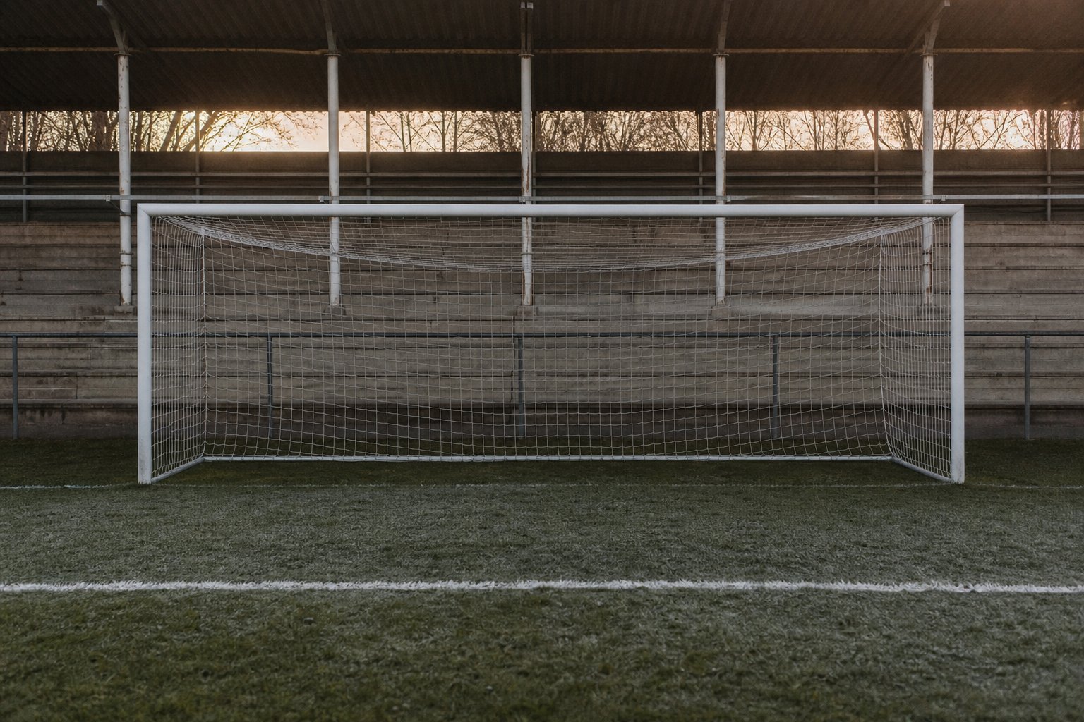 An empty goalmouth on a football pitch, the netting still and the goal line marked in front of it