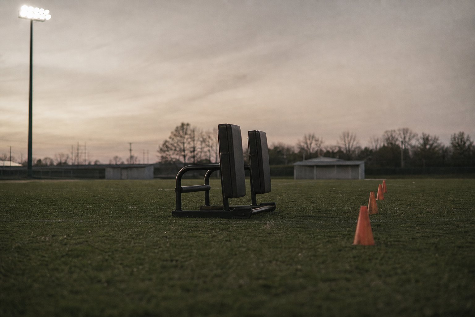 A blocking sled and a line of training cones on an empty practice field at dusk